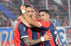 Jugadores de Cerro Porteño abrazan a su compañero tras un gol, con camisetas rojas y azules, en un estadio lleno de aficionados.
