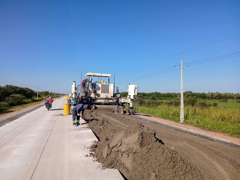 Trabajadores en uniforme de construcción manipulan concreto fresco; máquina pesada centra la imagen en ambiente rural y despejado.