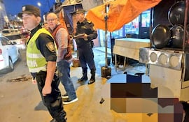 Dos policías con chalecos amarillos hablan con un civil en una calle comercial, rodeados de un ambiente tenso y vehículos estacionados.