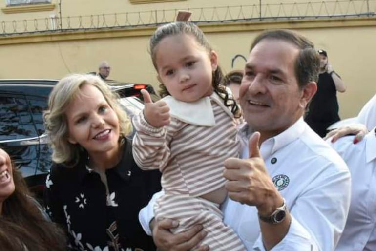 Arnaldo Samaniego con camisa blanca y una niña muestra pulgares hacia arriba, mientras una mujer sonriente los acompaña en fondo amigable.