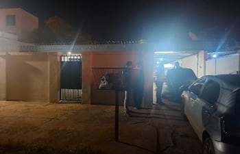 Tres personas, una con un objeto en mano, conversan en la oscuridad cerca de un vehículo y un edificio residencial.