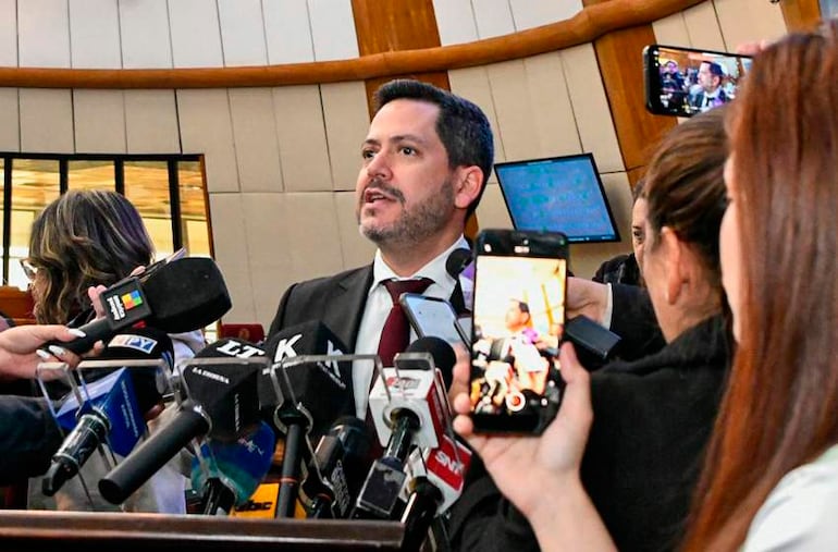 Raúl Latorre, en traje oscuro y corbata clara, habla rodeado de periodistas con micrófonos y cámaras.