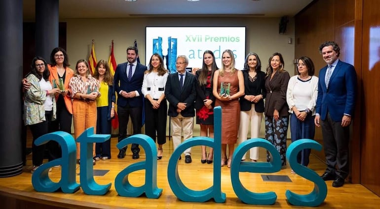 Catorce personas posan en un escenario con estatuillas en manos, todas vestidas formalmente, en ambiente festivo.