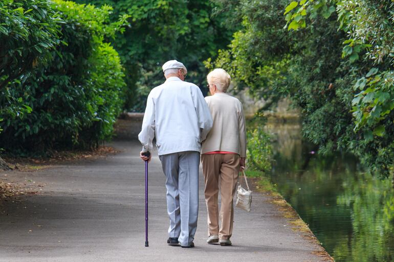 Una pareja de ancianos camina junto a un lago por un parque.