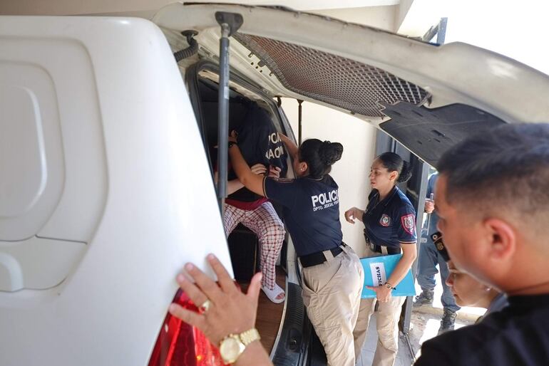 Agentes de policía ayudan a Dalia López Troche, vestida de pijama, cubriéndola con un saco oscuro junto a una furgoneta blanca.