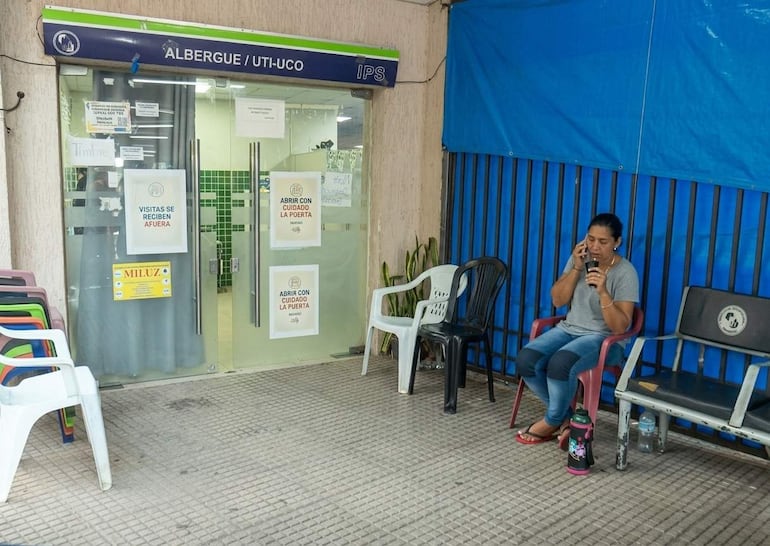 Mujer sentada en una silla, vestida con camiseta gris y jeans, habla por teléfono con expresión triste, junto a una botella de agua.