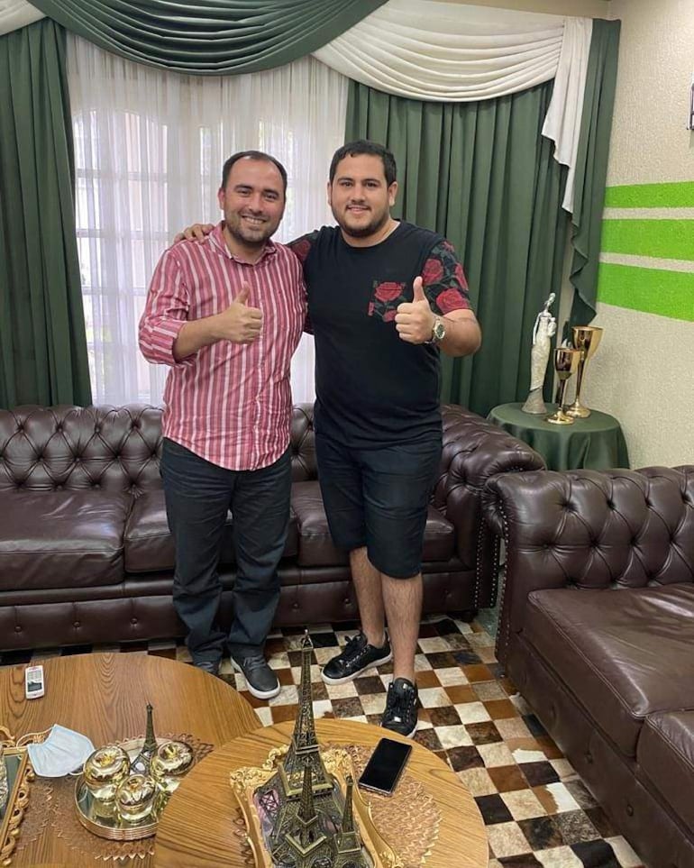 Jorge Bogarín en camisa de rayas y José Vázquez Acosta en camiseta negra, ambos sonriendo y levantando el pulgar en un salón con decoración elegante.