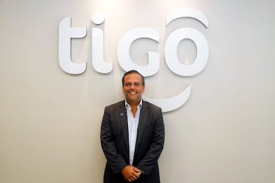 Marcelo Benítez, con traje oscuro y camisa blanca, sonríe frente al logo de Tigo en un ambiente corporativo.