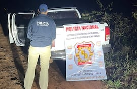 Agente de la Policía Nacional con abrigo azul de espaldas frente a camioneta con puerta abierta en camino rural.
