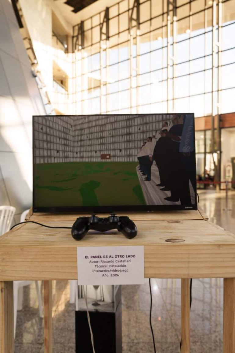 Instalación de Riccardo Castellani con una pantalla mostrando un videojuego sobre una mesa de madera en un entorno luminoso.