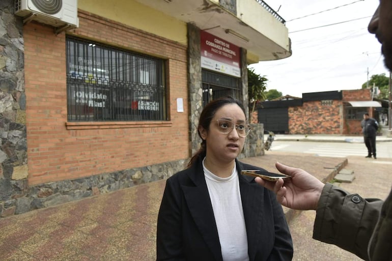Mujer con chaqueta negra y camiseta blanca, hablando con un hombre fuera del Centro Municipal Oñondivepa, observada por un policía.