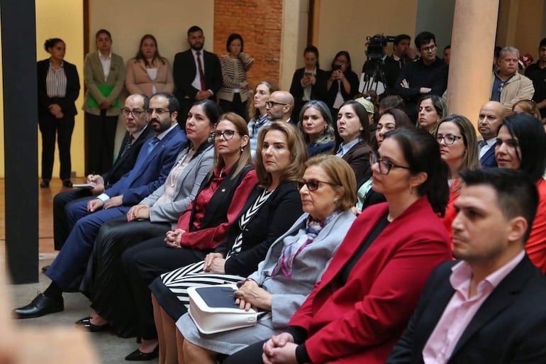 Alicia Pomata y Javier Dejesús Esquivel sentados en un evento formal, rodeados de mujeres con trajes formales y expresiones atentas.
