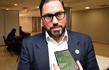 Gianmarco Felippo, con barba y gafas, vestido de saco oscuro, habla por teléfono en un ambiente profesional.