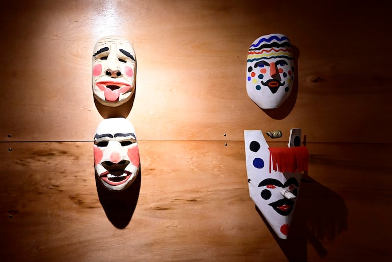 Máscaras artísticas con diseños coloridos, iluminadas en una pared de madera en un ambiente interior.