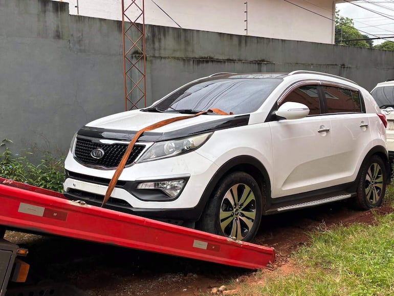 SUV blanco, posiblemente un Kia, siendo remolcado sobre plataforma roja en un ambiente exterior con fondo gris.