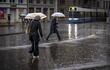 Personas caminan con paraguas mientras cruzan cerca de una conocida plaza en Zúrich (Suiza), en un día lluvioso.
