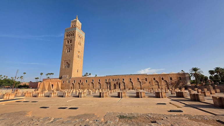 Torre de Koutoubia con detalles arquitectónicos, rodeada de palmeras y un cielo azul brillante.