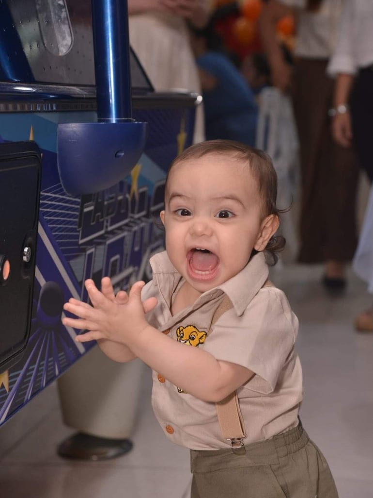 Niño de cabello rizado y oscuro, con camisa beige y tirantes, se divierte en un lugar de juegos infantiles.