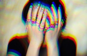 Persona sin identificar cubriendo su rostro con las manos, resaltando colores vibrantes y un ambiente de introspección.