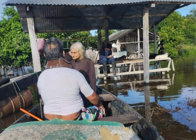 Un hombre en bote ayuda a una mujer cuya vivienda fue tomada por las aguas.