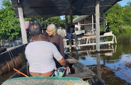 Un hombre en bote ayuda a una mujer cuya vivienda fue tomada por las aguas.