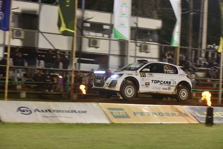 Coche blanco con el número 51 en pleno salto, rodeado de espectadores entusiastas y carteles publicitarios en un ambiente de rally.