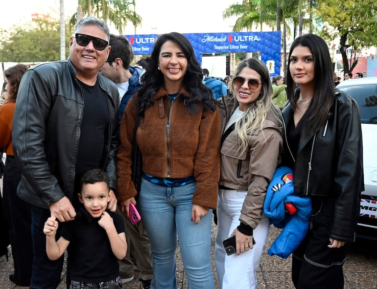 Hombre canoso con gafas sonríe junto a un niño, y tres mujeres se agrupan, todas con chaquetas en un ambiente festivo.
