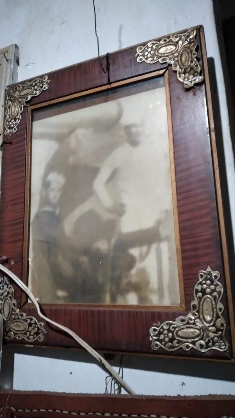 Sixto Sosa Ramírez, nonagenario, se encuentra frente a un marco de foto antiguo en un ambiente doméstico con estilo histórico.