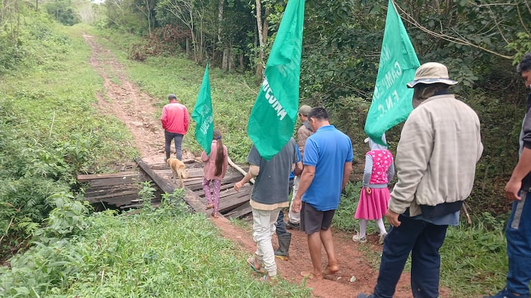 Grupo de personas, entre ellos una niña con camiseta de rayas, marchan con banderas verdes en un sendero rodeado de vegetación.