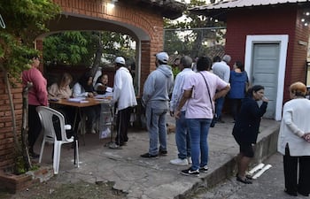 Grupo de personas en la entrada de un local de votación, con dos mujeres sentadas y un hombre de pie entregando documentación.