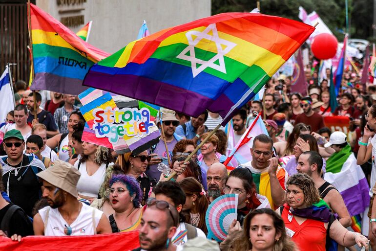 Una bandera con los colores del arcoiris y la estrella de David flamea sobre los participantes de la marcha del orgullo. 