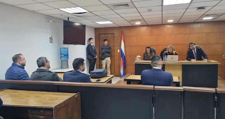 Un tribunal con cuatro personas al frente, incluyendo mujeres y hombres, y una bandera de Paraguay visible en el fondo.
