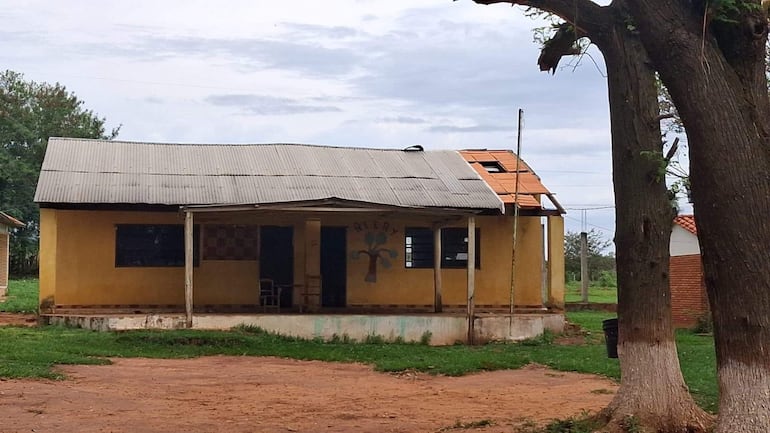 Construcción de una planta con techo dañado y fachada amarilla, ubicada en un área rural sin personas visibles.
