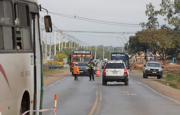 Agente de tránsito con uniforme amarillo y negro y trabajador en chaleco naranja dirigen el tráfico en una carretera urbanizada.