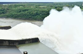 Represa de Itaipú vertiendo agua en un entorno natural de vegetación densa, bajo un cielo nublado.