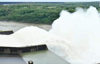 Represa de Itaipú vertiendo agua en un entorno natural de vegetación densa, bajo un cielo nublado.