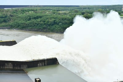 Represa de Itaipú vertiendo agua en un entorno natural de vegetación densa, bajo un cielo nublado.