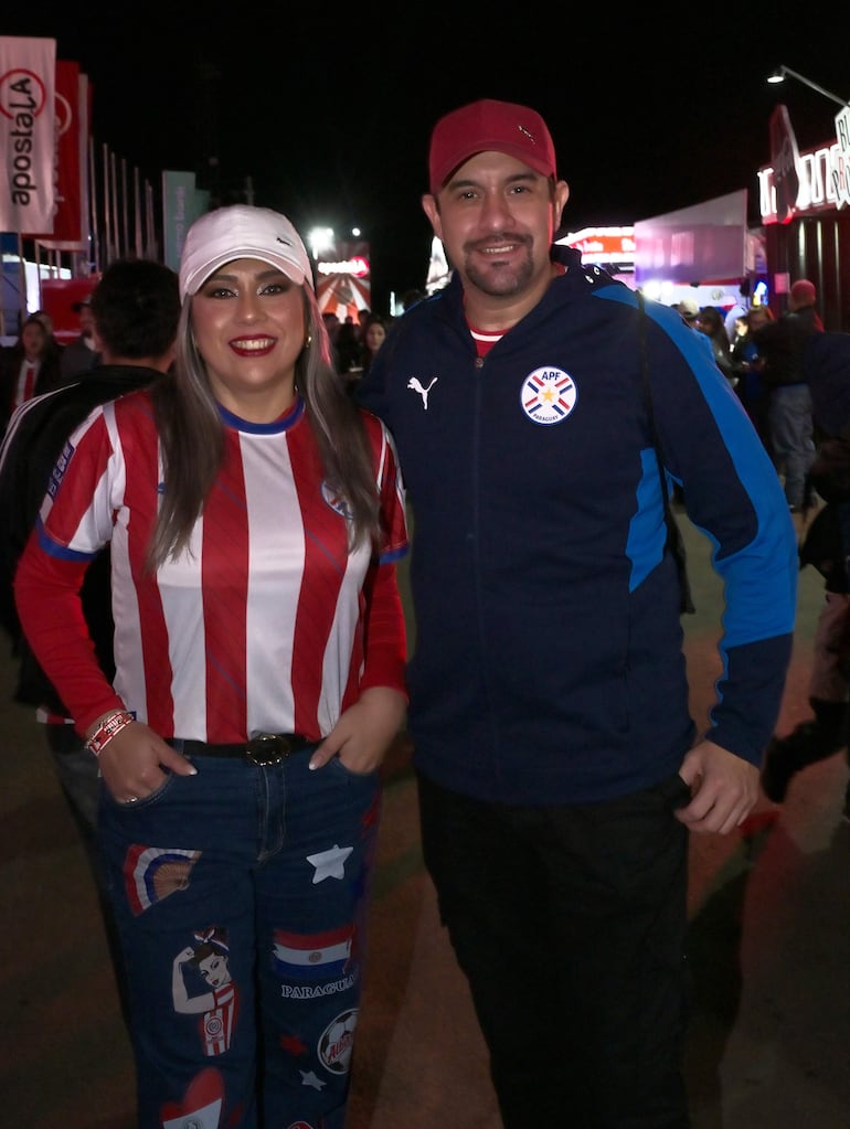 Mujer con camiseta a rayas rojas y blancas y hombre en chaqueta oscura con escudo de la APF, sonríen en ambiente iluminado.
