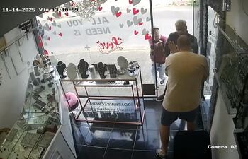 Instante en que los asaltantes sorprenden al dependiente cuando les abre la puerta del negocio y luego es reducido.