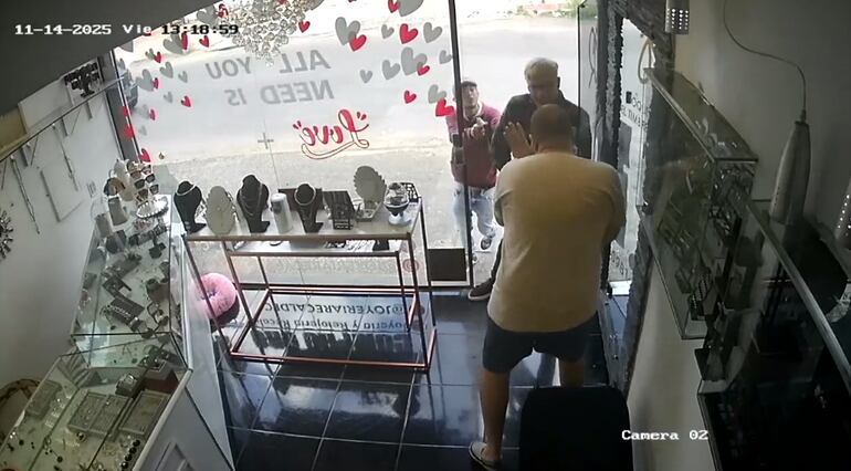 Instante en que los asaltantes sorprenden al dependiente cuando les abre la puerta del negocio y luego es reducido.