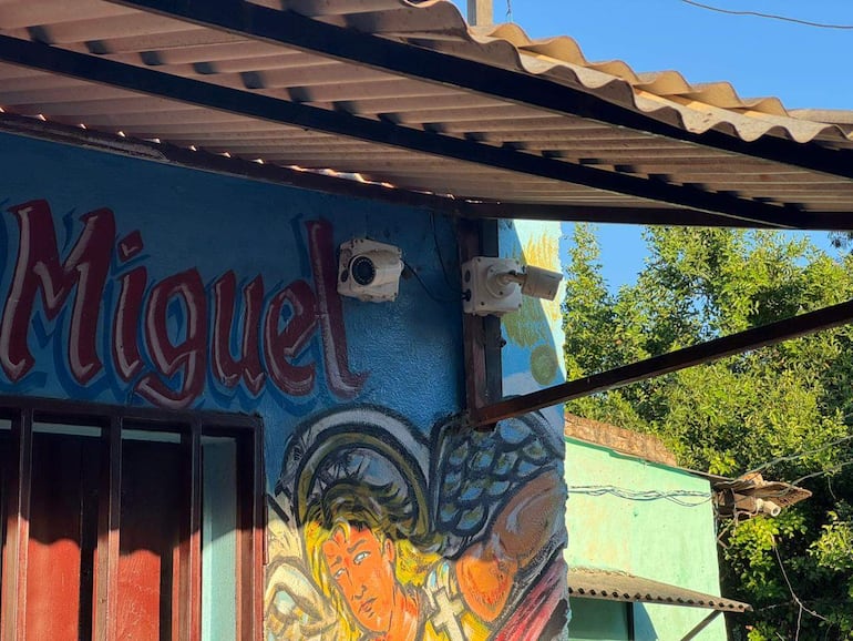 Fachada de un edificio con mural colorido de un ángel y cámaras de vigilancia visibles en la pared.