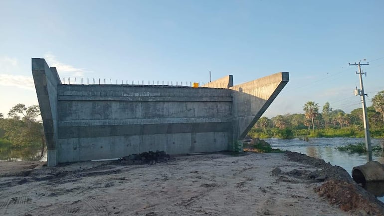 Estructura de un puente en construcción rodeada de vegetación y agua, sin personas visibles en una escena soleada.