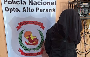 Individuo con prenda oscura de espaldas frente a cartel de Policía Nacional en un ambiente cerrado.