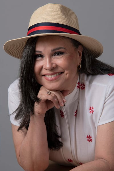 Lizza Bogado, mujer de cabello oscuro y largo, sonríe con un sombrero de paja y blusa blanca con bordados rojos.