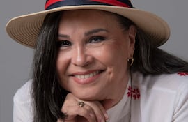 Lizza Bogado, mujer de cabello oscuro y largo, sonríe con un sombrero de paja y blusa blanca con bordados rojos.