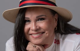 Lizza Bogado, mujer de cabello oscuro y largo, sonríe con un sombrero de paja y blusa blanca con bordados rojos.