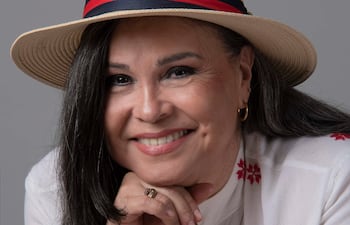 Lizza Bogado, mujer de cabello oscuro y largo, sonríe con un sombrero de paja y blusa blanca con bordados rojos.