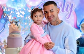 Derlis González sonríe mientras sostiene a una niña con vestido rosa, rodeados de decoraciones festivas y un pastel de cumpleaños.