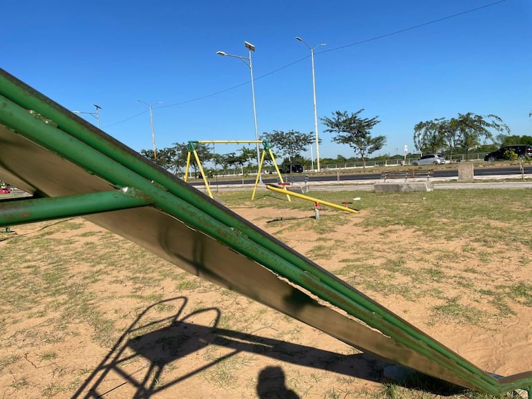 Área recreativa desierta en Asunción, con tobogán verde y columpio amarillo en un entorno de césped y arena.
