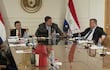 Dionisio Amarilla gesticula mientras Celeste Amarilla escucha atentamente en un ambiente formal con una bandera paraguaya detrás.